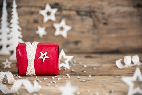 Ein kleines, rot verpacktes Weihnachtsgeschenk liegt auf einer Holzauflage. 