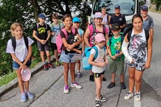 Auf dem Bild sind 9 Kinder und 3 Erwachsene als lockere Gruppe zu sehen. Im Hintergrund ist der weiße City Bus der Stadt.