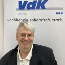 Auf dem Bild ist ein Mann mit kurzen grauen Haaren, Brille, wei&szlig;em Hemd und schwarzem Jackett zu sehen