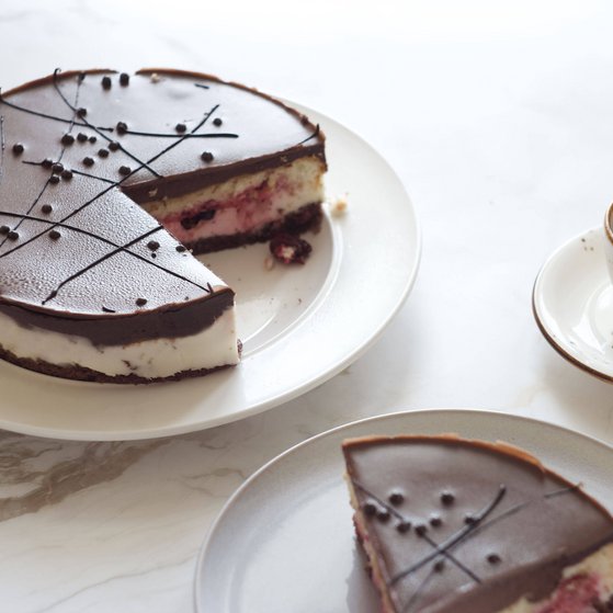 In der Mitte steht ein angeschnittener Schoko-Sahne-Kuchen. Rechts daneben steht eine Tasse Kaffee. Davor steht ein Teller mit einem St&uuml;ck Kuchen. 