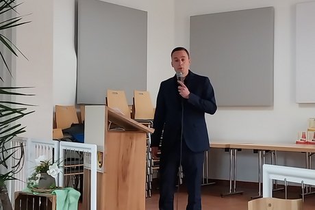 Redner steht mit dem Mikrofon in der Hand an einem Vortragspult und spricht.