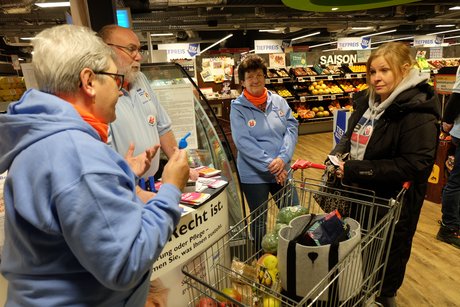 Die VdK Vorstandsmitglieder am Infostand im Rewe Markt mit einer Interessentin
