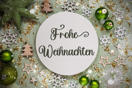 Grafik mit weihnachtlicher Deko und dem Text „Frohe Weihnachten“.