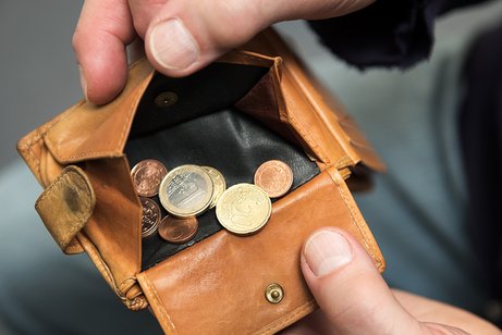 H&auml;nde eines Mannes halten eine Geldb&ouml;rse offen, darin befinden sich wenige M&uuml;nzen. 