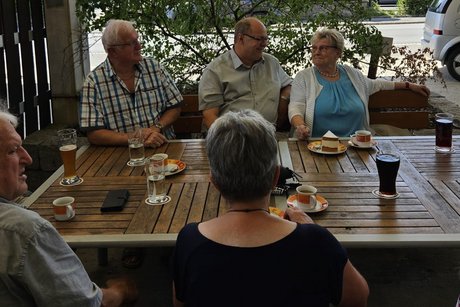 8 Personen sitzen am Tisch im Biergarten und haben Getr&auml;nke vor sich