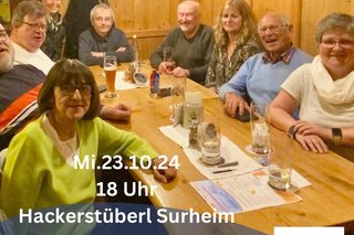 Menschen sitzen um Tisch. Auf dem Bild steht ein Text zum nächsten Stammtisch