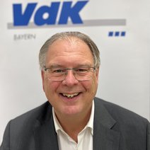 Auf dem Bild ist ein Mann mit kurzen grauen Haaren, Brille, wei&szlig;en Hemd und grauen Jackett zu sehen