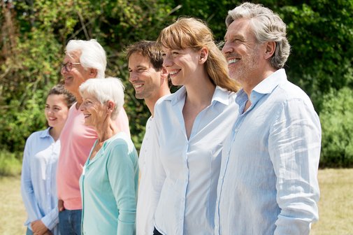 Eine Gruppe aus jungen und alten M&auml;nnern und Frauen stehen nebeneinander, blicken l&auml;chelnd in die Ferne. 