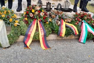 Verschiedene Kränze mit Schleifen liegen auf Sockel aus Beton