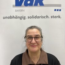 Auf dem Bild ist eine Frau mit zusammengebundenen Haaren, Brille, braunem Kragen und schwarzem Pulli zu sehen.