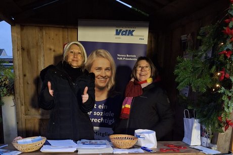 Zwei Frauen stehen in einer Weihnachtsbude und geben Auskunft. Dick eingepackt und mit Nikolausm&uuml;tze zeigt Conni Albrecht, Angestellte im VdK Ingolstadt Eichst&auml;tt, die Daumen hoch. Daneben Edith Rixner, Ehrenamtliche Pflegebegleiterin.