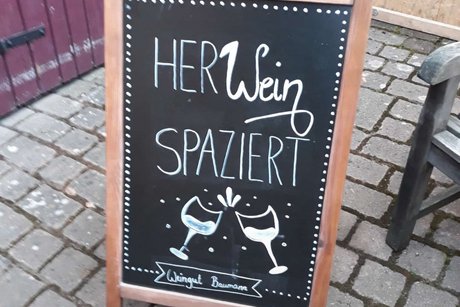 Foto eines Kundenstoppers mit der Aufschrift "Her Wein spaziert" im Eingangsbereich der Wirtschaft