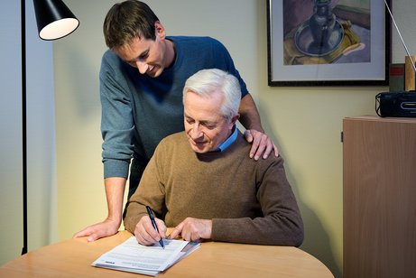 Ein &auml;lterer Mann sitzt an einem K&uuml;chentisch und f&uuml;llt eine VdK-Beitrittserkl&auml;rung aus, ein j&uuml;ngerer Mann blickt ihm &uuml;ber die Schulter.