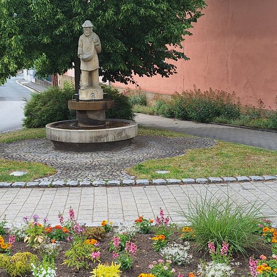 Auf dem Bild ist der S&auml;mannbrunnen von Ebensfeld zu sehen. Davor ist ein Blumenbeet