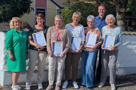 Die Jubilare stehen mit der Kreisgesch&auml;ftsf&uuml;hrerin und dem B&uuml;rgermeister vor einer Mauer, im Hintergrund sind B&auml;ume
