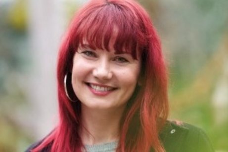 Zu sehen ist ein Portrait von Frau Dr. Sarah Straub, l&auml;chelnd und mit r&ouml;tlich gef&auml;rbten nackenlangen Haaren.