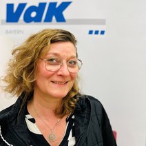 Auf dem Bild ist eine Frau mit kinnlangen gelockten blonden Haaren, Brille und schwarzem Oberteil zu sehen