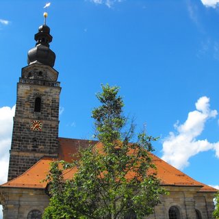 Bild zeigt die das Wahrzeichen von St. Georgen. Die Ordenskirche. Zu sehen ist die Ansicht vom Parkplatz hinter der Kirche mit einem Baum im Vordergrund bei Sonnenschein und einem blauen Himmel mit einigen Wolken.