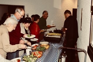 Menschen stehen beim Buffet und holen sich auf Tellern Salat und warmes Essen