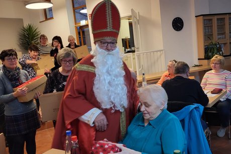 Der Nikolaus gibt ein Geschenk an eine Frau aus, die an einem Tisch sitzt.