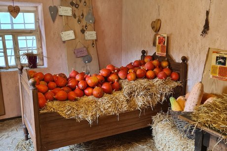 Zimmer im kleinen Kürbishaus Es steht ein altes, dunkles Holzbett mit Stohballen in einem kleinen Zimmer vom kleinen Kürbishausgefüllt und darauf jede Menge Hokaidokürbissen