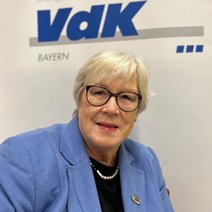 Auf dem Bild ist eine Frau mit grauen Haaren, Brille und blauen Blazer zu sehen.