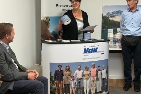 Susann Enders, Kreisvorsitzende VdK-Oberland, an VdK-Theke mit goldener Klopapierrolle