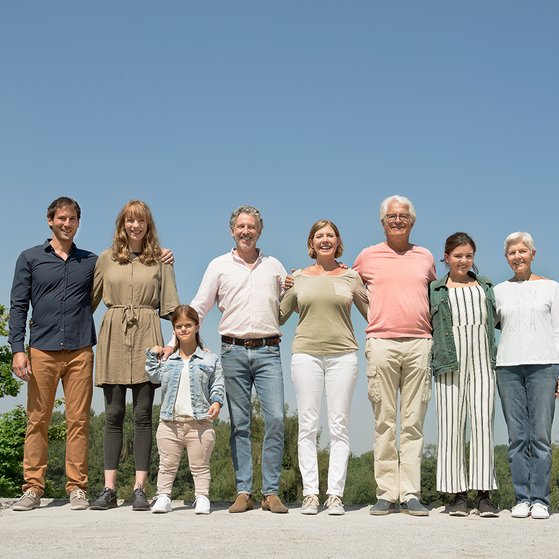 Menschen verschiedenen Alters mit und ohne Behinderung stehen untergehakt und l&auml;chelnd in einer Reihe in der Sonne