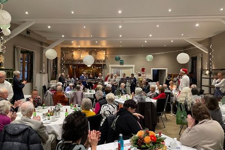 Saal mit vielen Gästen an Tischen und Posaunenchor