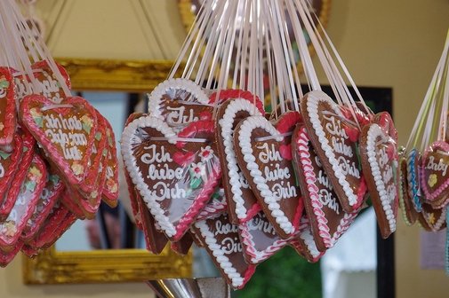 Es ist ein Stand mit vielen beschrifteten bunten Lebkuchenherzen zu sehen, wie man sie auf Volksfesten findet.