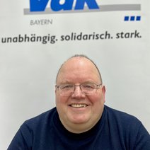 Auf dem Bild ist ein Mann mit kurzen Haaren, Brille und blauem Pullover zu sehen.