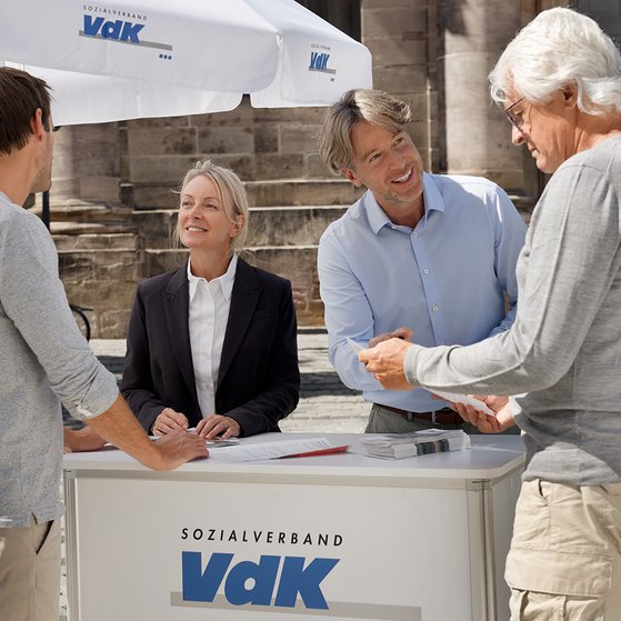 Eine Mitarbeiterin und ein Mitarbeiter an einem VdK-Infostand informieren gerade zwei interessierte Passanten. 