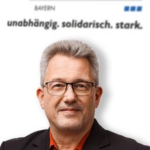 Auf dem Bild ist ein Mann mit kurzen grauen Haaren mit rotem Hemd und schwarzen Jackett zu sehen