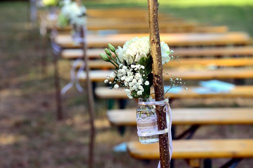 unscharf im Hintergrund mehrere Bierzeltgarnituren im Vordergrund ein Glas mit wei&szlig;en Blumen