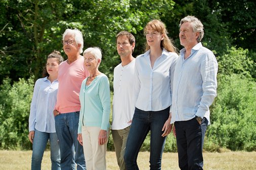 Eine Gruppe aus jungen und alten M&auml;nnern und Frauen stehen nebeneinander, blicken ernst in die Ferne. 