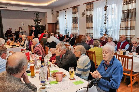 Teilnehmer der Weihnachtsfeier sitzen am Tisch und hören die Rede des Vorsitzenden