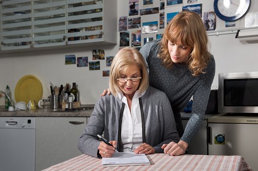 Eine &auml;ltere Frau sitzt an einem Tisch, f&uuml;llt eine VdK-Beitrittserkl&auml;rung aus, eine j&uuml;ngere Frau blickt ihr &uuml;ber die Schulter. 