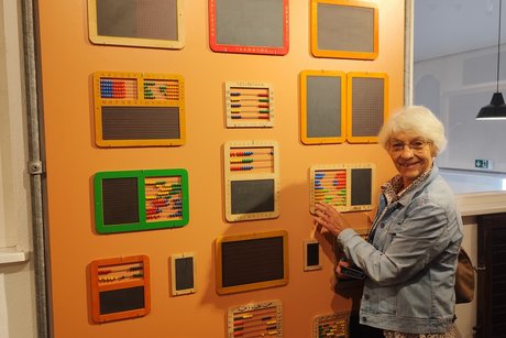 Eine der Teilnehmenden schaut sich die früheren Rechenmaschinen mit Kugeln auf den Linien genauer an.