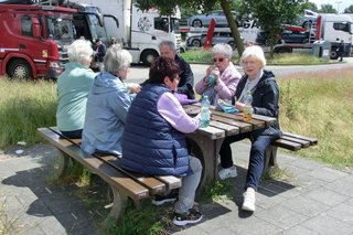 Auf dem Bild: Fünf Frauen und ein Mann, sitzen auf Bänken und halten letzte Rast auf der Heimreise.