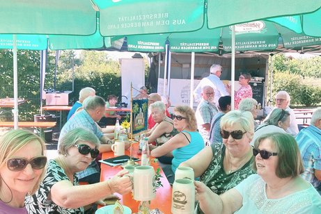 Gäste sitzen bei strahlendem Sonnenschein zum Kaffeekränzchen an Biertischen und unterhalten sich.