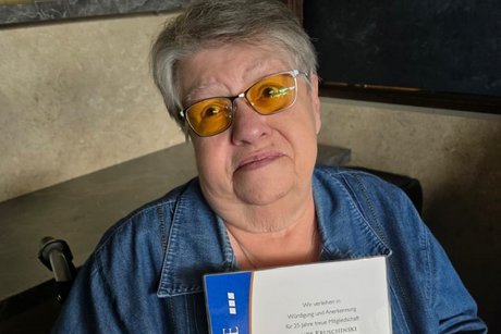 Renate Kruschinski, eine Jubilarin, sitzt im Rollstuhl und h&auml;lt die Urkunde vor sich
