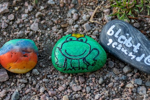 drei bemalte Steine- einer bunt, ein gr&uuml;ner mit Frosch und einer mit der Beschriftung- bleibt gesund