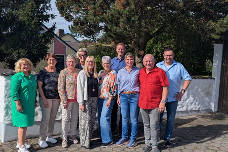 Die Vorstandschaft steht mit der Kreisgesch&auml;ftsf&uuml;hrerin und dem B&uuml;rgermeister vor einer Mauer, im Hintergrund sind B&auml;ume