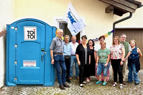 Barrierefreie mobile Toilette neben einer Gruppe Menschen, VdK-Flagge
