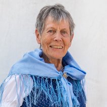 Wilma Frömmel, Frauenbeauftragte des VdK Ortsverbands Aubing, steht vor einem hellen Hintergrund und lächelt freundlich in die Kamera. Sie trägt ein traditionelles dunkelblaues Dirndl mit weißer Bluse und ein hellblaues Fransentuch, das über ihre Schultern gelegt ist. Ihre Haltung ist aufrecht und offen.