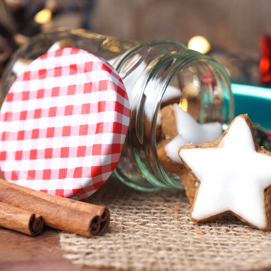 Die Weihnachtzeit naht Auf einem Tisch liegt ein Weckglas, das mit Zimtsternen gefüllt ist. Links daneben liegen drei Zimtstangen.
