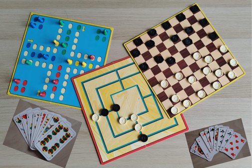 Bild zeigt drei Brettspiele mit Spielsteinen (Mensch &auml;rger dich nicht, Damespielbrett und M&uuml;hlenspielbrett) und zwei Kartenspielbl&auml;tter Skat und Schafkopf auf einem Tisch.