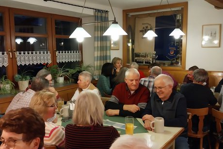 G&auml;ste sitzen an mehreren Tischen in der Gaststube und unterhalten sich.