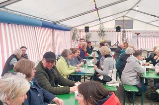 Gäste sitzen im Bierzelt an Biertischen und unterhalten sich.