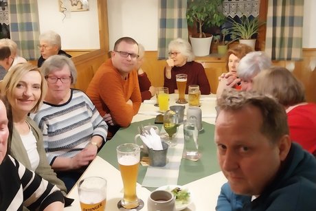 G&auml;ste sitzen an einem langen Tisch im Lokal und unterhalten sich.